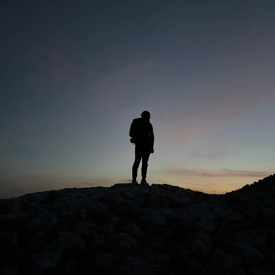 A silhouetted hiker on a rocky summit at dusk on Visočica